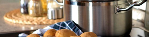 An image of a pile of potates in a kitchen, next to a cooking pot.