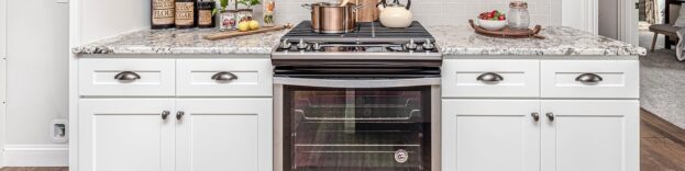 An image of a modern kitchen with white cupboards and work surfaces. In the middle of the image, there is an oven.